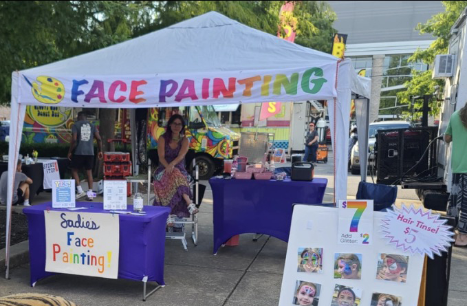 Sadie's Face Painting booth setup at a festival with design menu and pricing