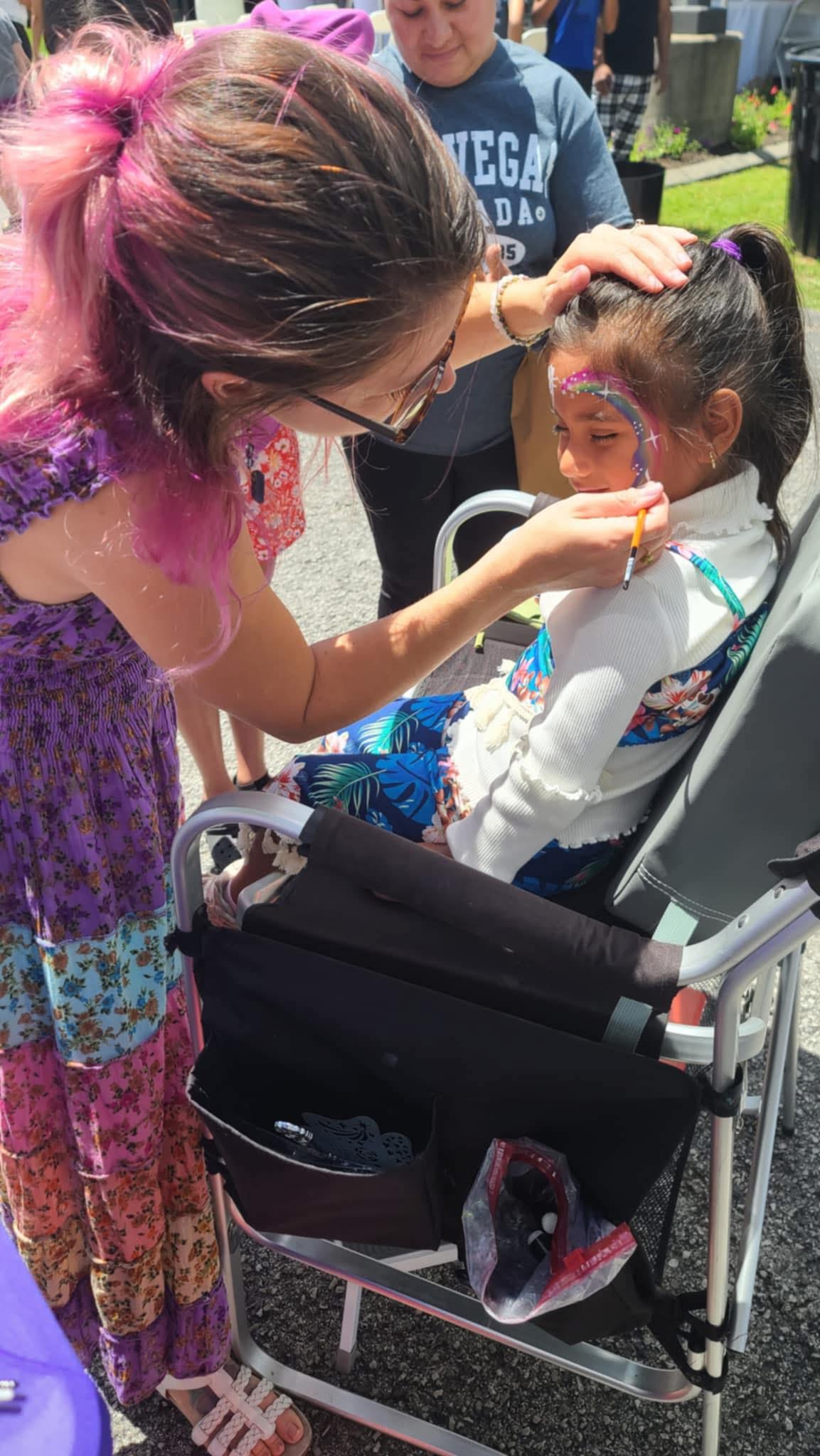 Sadie painting a fairy design on a child at an outdoor event