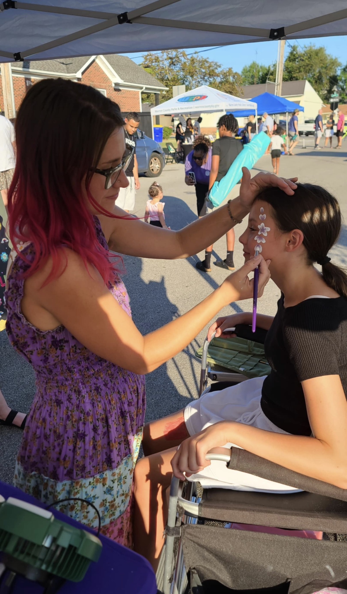 Sadie carefully painting flowers on a girl's face at a community event